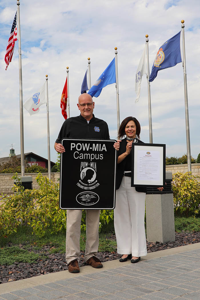 Man and woman in front of flags holding POW MIA sign.